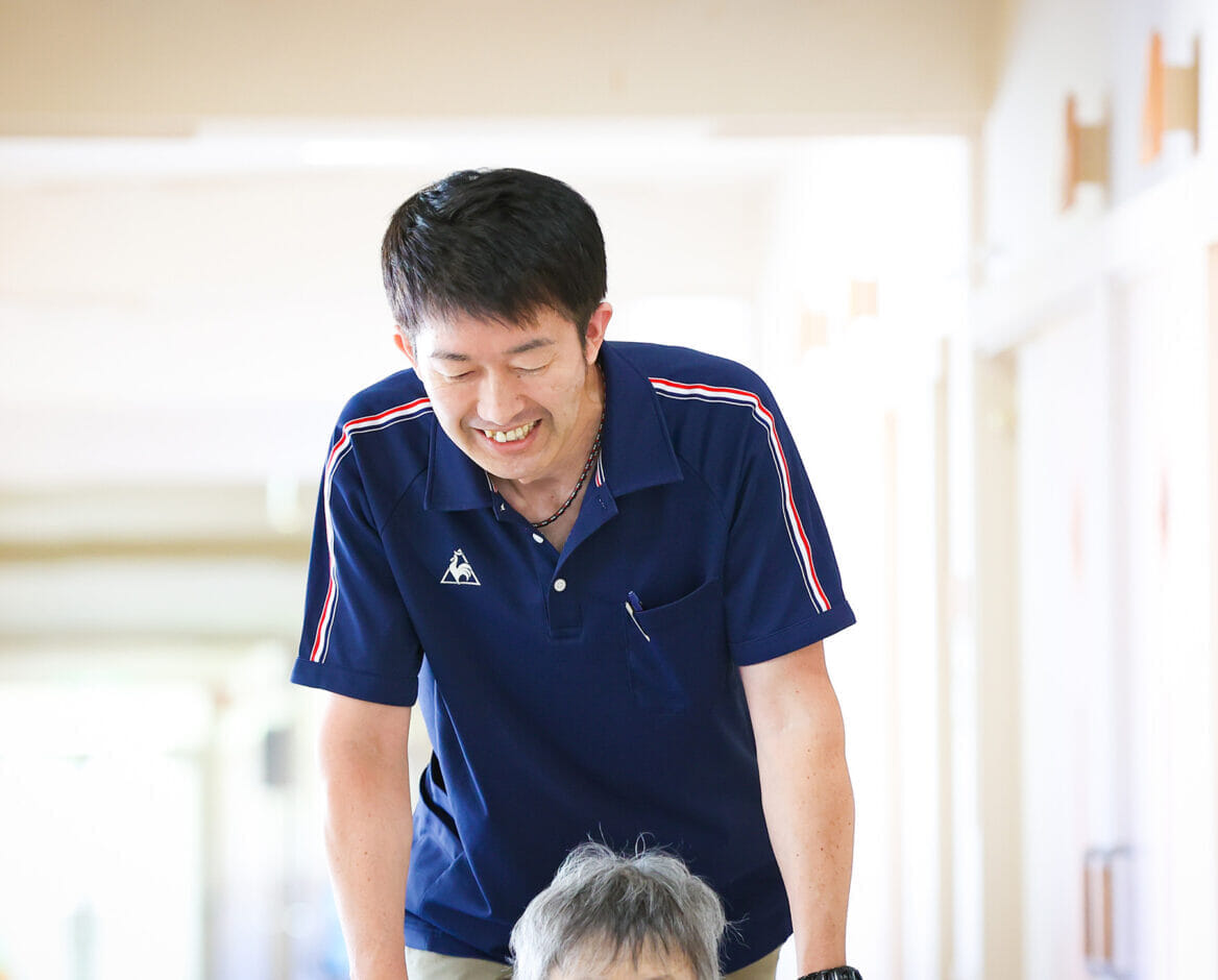 スタッフが入居者と笑顔で交流している様子。施設内の廊下で撮影。