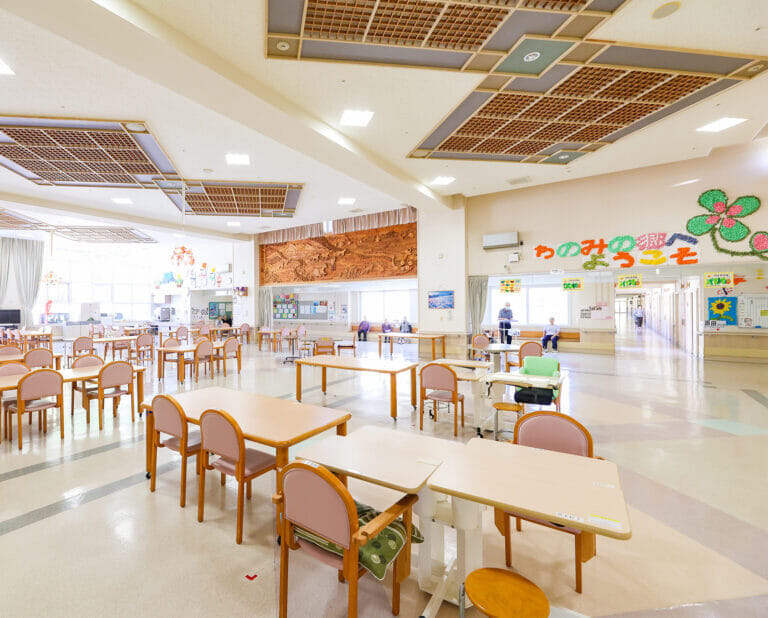 介護施設の広々とした食堂。テーブルと椅子が配置され、採光良好で明るい空間。